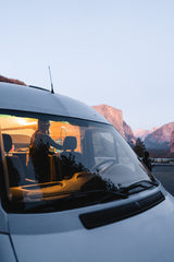 Experience van life freedom! Inside this RV rental, someone prepares a meal, with stunning mountain views through the windshield.