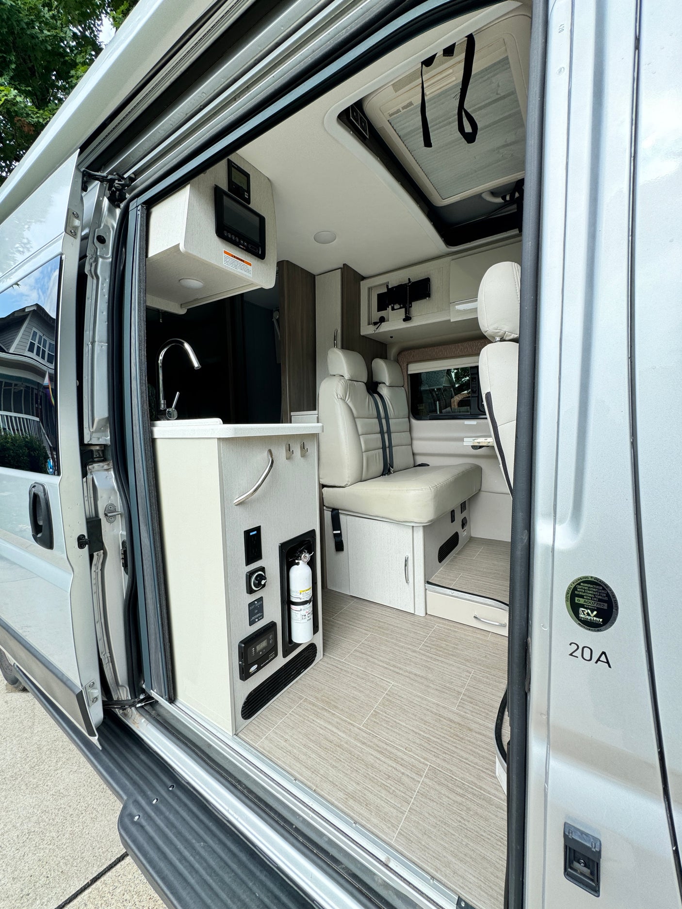 Step inside this modern RV rental: a compact kitchen, dinette seating, control panels, and fire extinguisher viewed through the open side door.