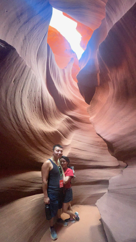 RV rental exploration: Couple smiles in a vibrant slot canyon with swirling sandstone walls and light shafts from above.