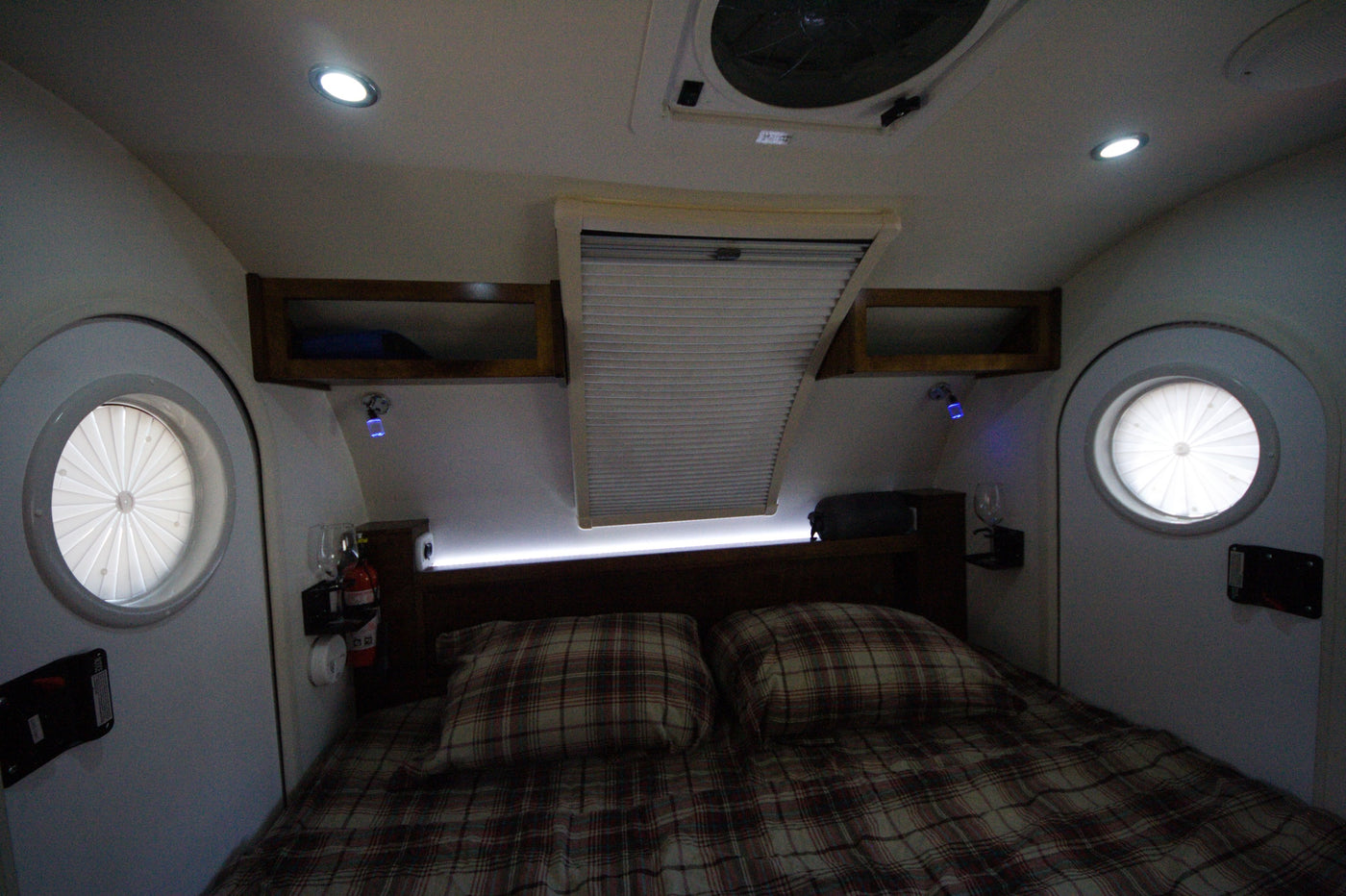 Cozy RV rental interior featuring a plaid bed, circular windows, and overhead storage for comfortable travel. — photo 11