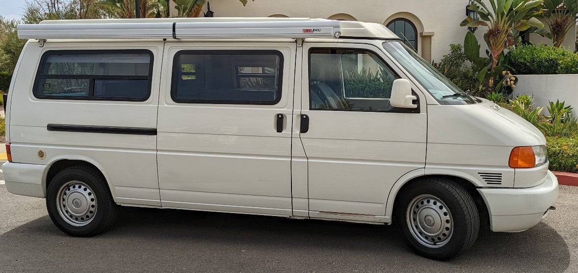 Experience adventure in this white VW T4 camper van, featuring a pop-top roof and awning, ideal for your next RV rental.