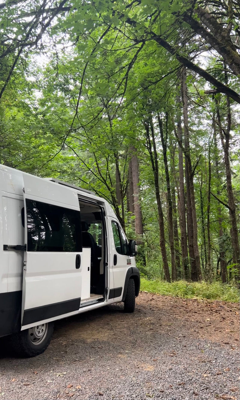 White RV rental van on a gravel forest path, side door open. Surrounded by tall green trees, ready for adventure. — photo 17