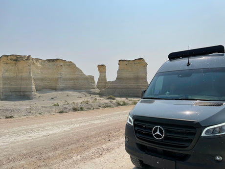 An RV rental, a Mercedes-Benz Sprinter van, parked on a dirt road facing impressive light-colored chalk formations.