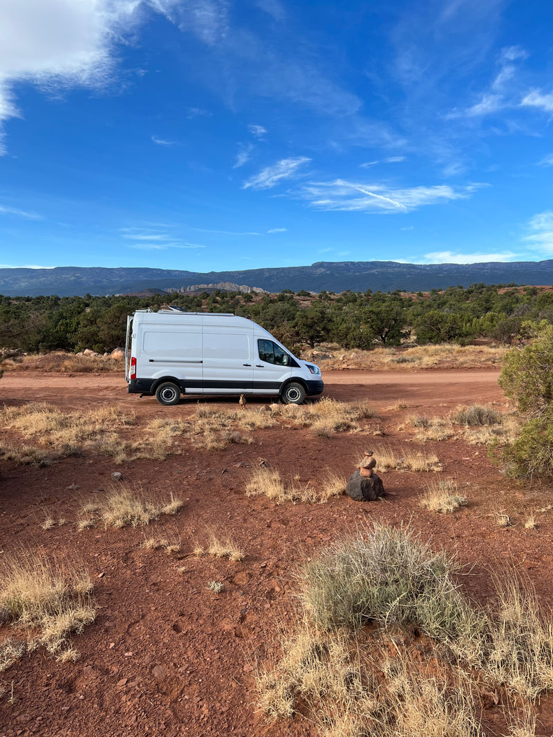 White campervan RV rental parked on a red dirt road, surrounded by desert brush and distant mountains under a blue sky. — photo 10