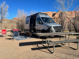 Scenic RV rental campsite: A silver camper van parked, with chairs, picnic table, and desert mountains.