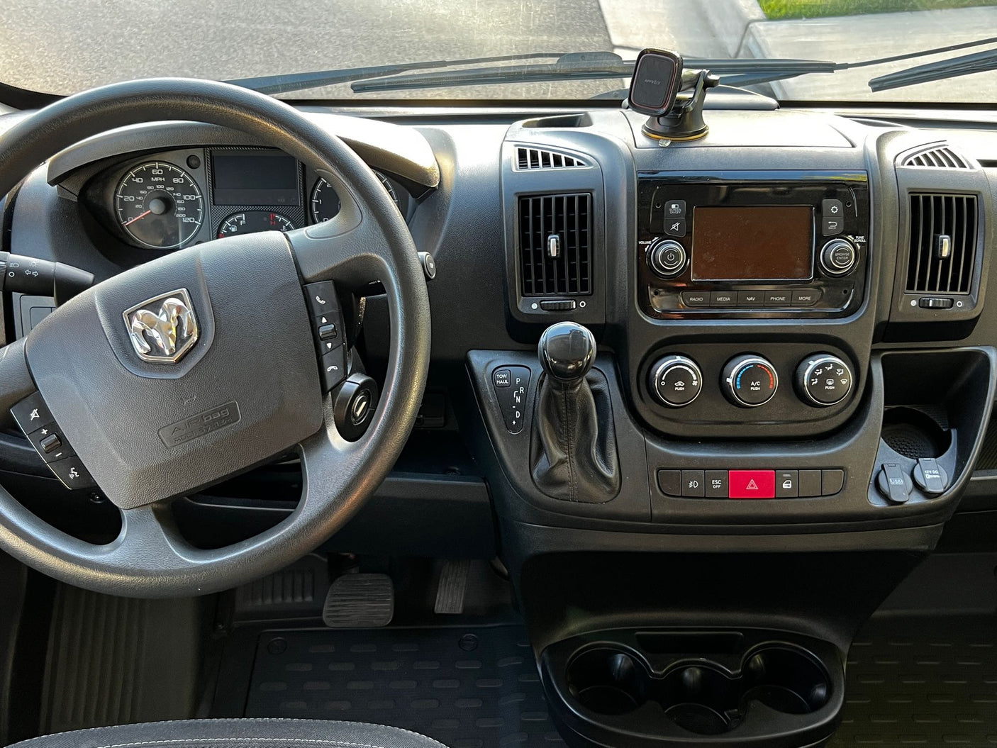 Detailed view inside an RV rental van: driver's dashboard, steering wheel, media console, climate controls, and gear shifter.