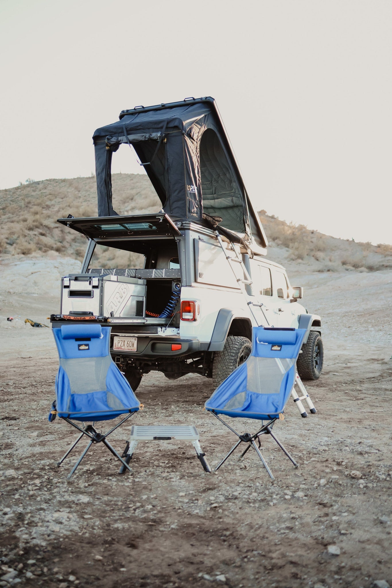 Explore the outdoors! This white off-road vehicle with a rooftop tent and camping chairs is an ideal rv rental setup. — photo 10