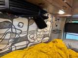 Cozy rv rental interior: yellow bedding, rolled black window shades, and a patterned fabric wall.