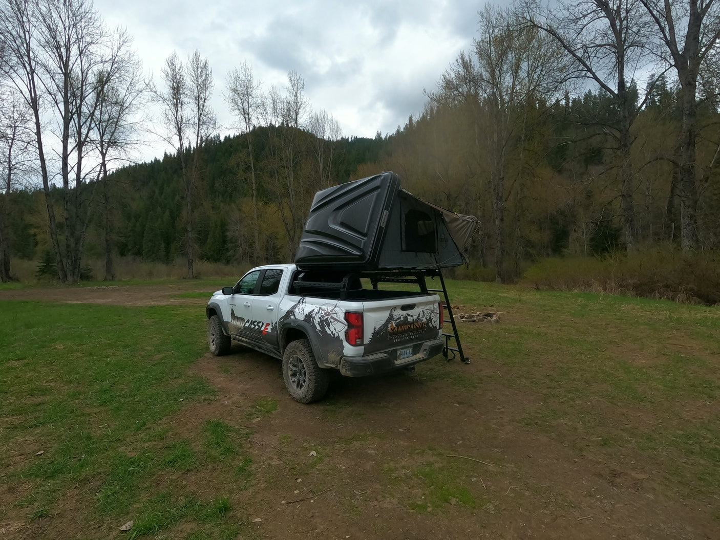 Overland RV rental pickup truck with rooftop tent set up at a forest campsite, ready for adventure.