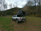 Overland RV rental pickup truck with rooftop tent set up at a forest campsite, ready for adventure.