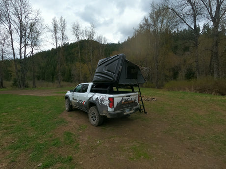 Overland RV rental pickup truck with rooftop tent set up at a forest campsite, ready for adventure.