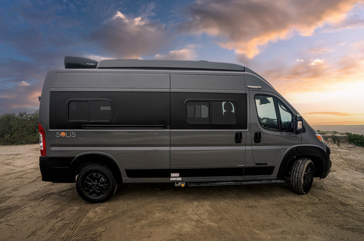 Gray Solis camper van for RV rental, parked on sand at sunset. Perfect for adventure travel & road trips.