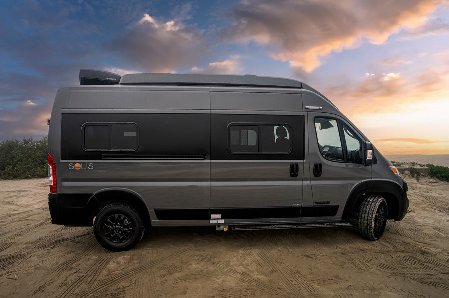 Gray Solis camper van for RV rental, parked on sand at sunset. Perfect for adventure travel & road trips.