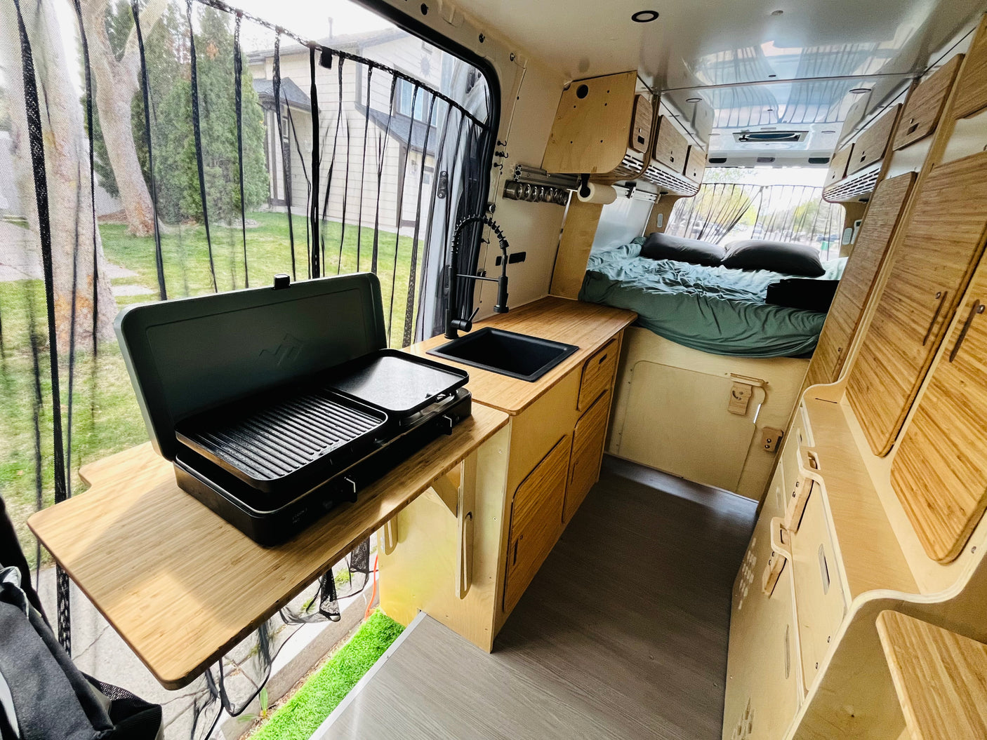 Inside a modern rv rental camper van: custom kitchen with sink & stove, comfortable bed, and clever wooden storage.