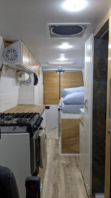 Inside a neat rv rental: compact kitchen with stove, wooden counters, a comfortable bed, and wood flooring.