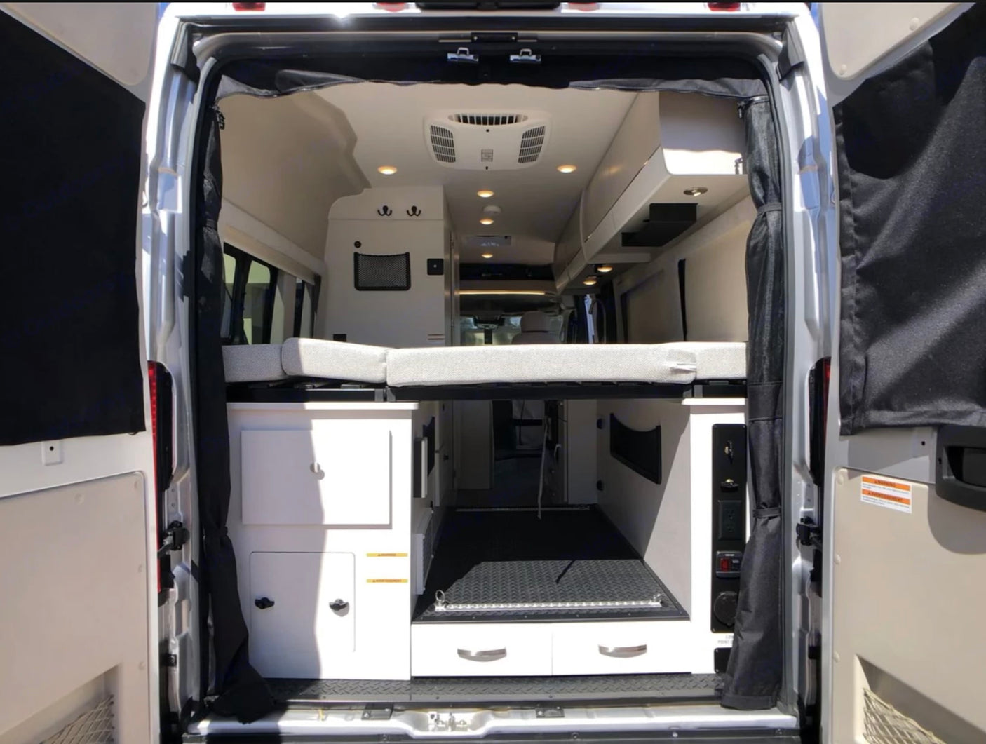 Explore this rv rental's spacious interior from the rear: elevated bed, storage, and cargo area. Ideal for road trips.