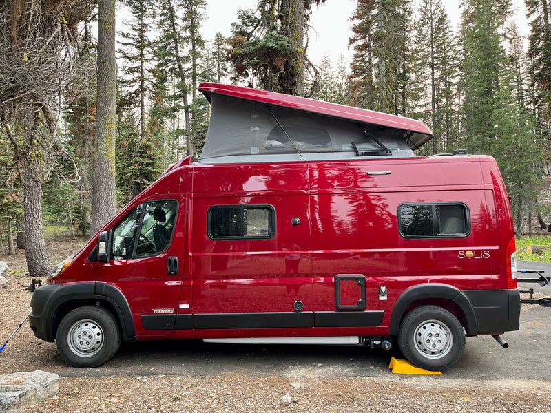  and a view of the outdoors with trees and people.|Red Winnebago Solis RV rental with pop-top raised — photo 8