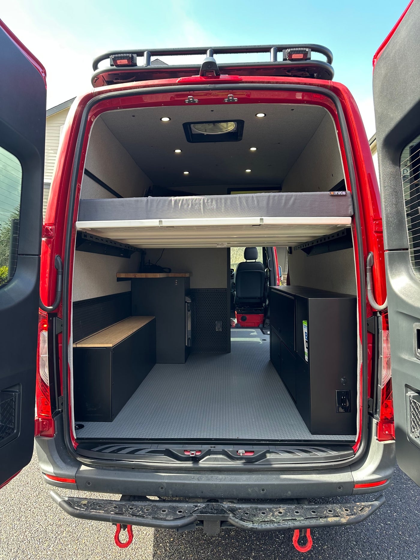 Spacious red camper van interior for your next RV rental adventure, featuring a raised bed and storage. — photo 4