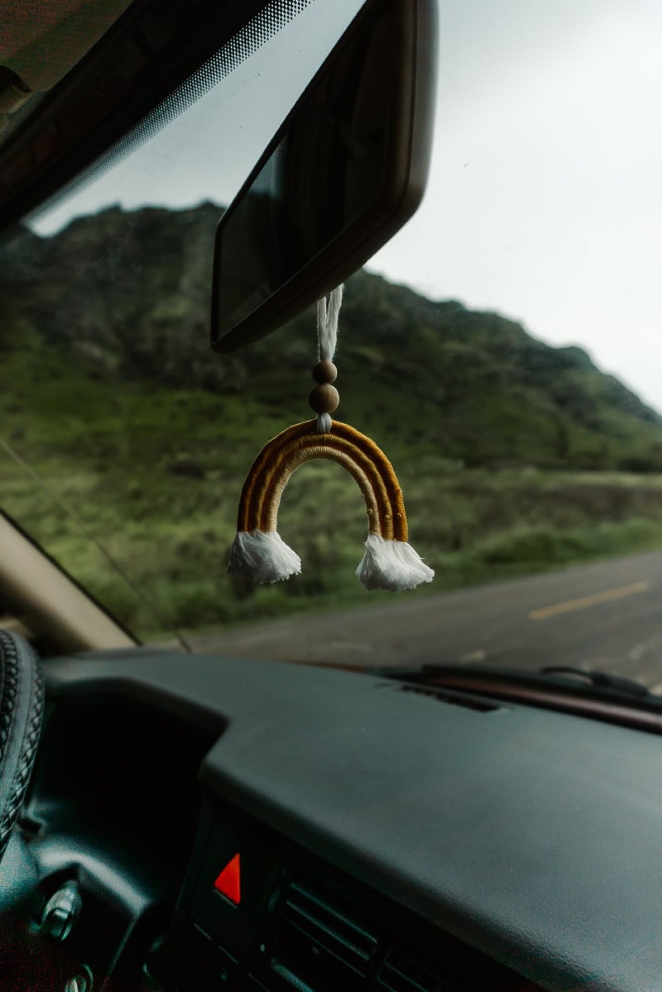 Road trip vibes: A rainbow charm hangs from the rearview mirror of an RV rental, overlooking green mountains.