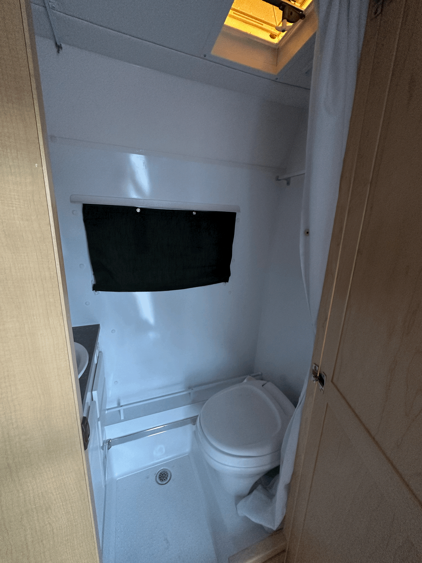 Inside an RV rental: a compact bathroom featuring a toilet, shower, small sink, and overhead vent/skylight.