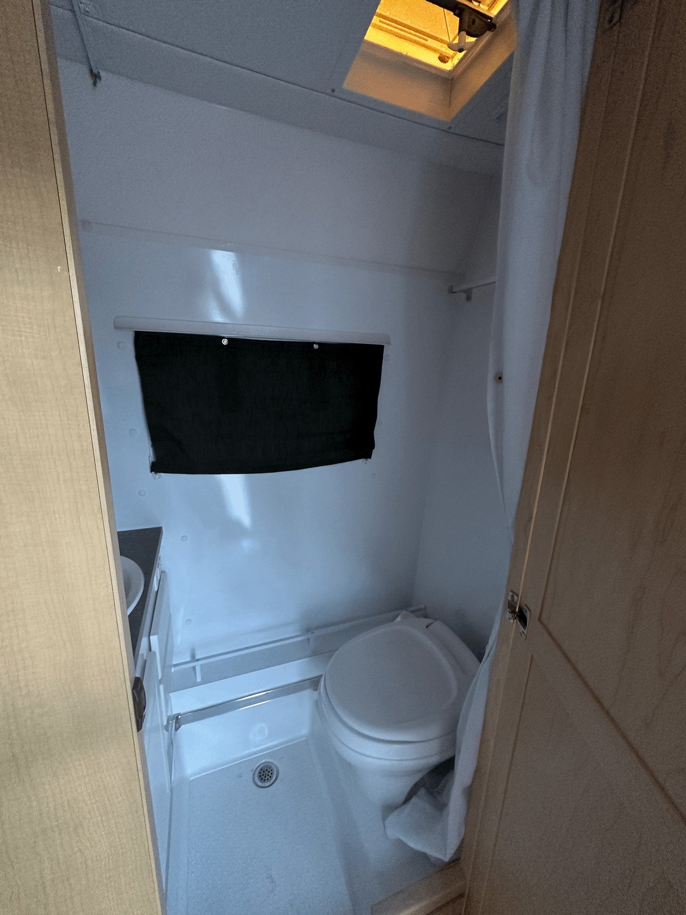 Inside an RV rental: a compact bathroom featuring a toilet, shower, small sink, and overhead vent/skylight. — photo 7
