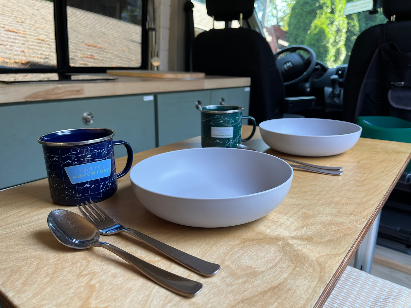 RV rental: Two mugs, bowls, and silverware on a wooden counter, ready for a meal in this cozy camper kitchen.