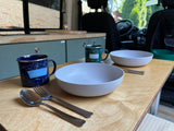 RV rental: Two mugs, bowls, and silverware on a wooden counter, ready for a meal in this cozy camper kitchen.