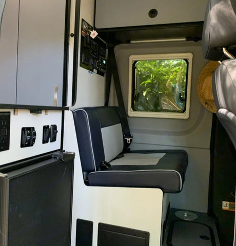 RV rental: Modern camper van interior with comfy bench seating, control panels, power outlets, and a window view of nature.