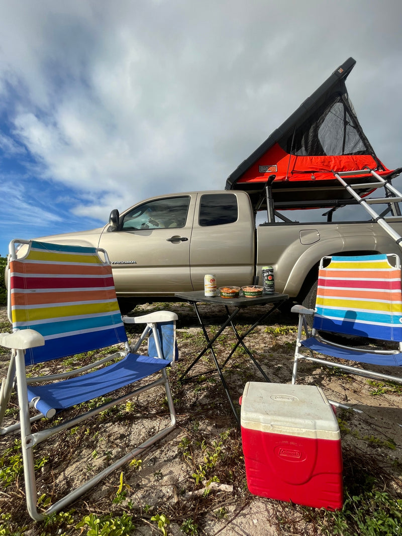 A tan truck with a rooftop tent, camp chairs, cooler, and table. An outdoor adventure awaits! Consider this an RV rental alternative. — photo 17