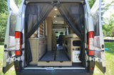 Inside an RV rental: rear view with open doors, mesh screen, convertible bed, storage, and utility panel for mobile adventures.