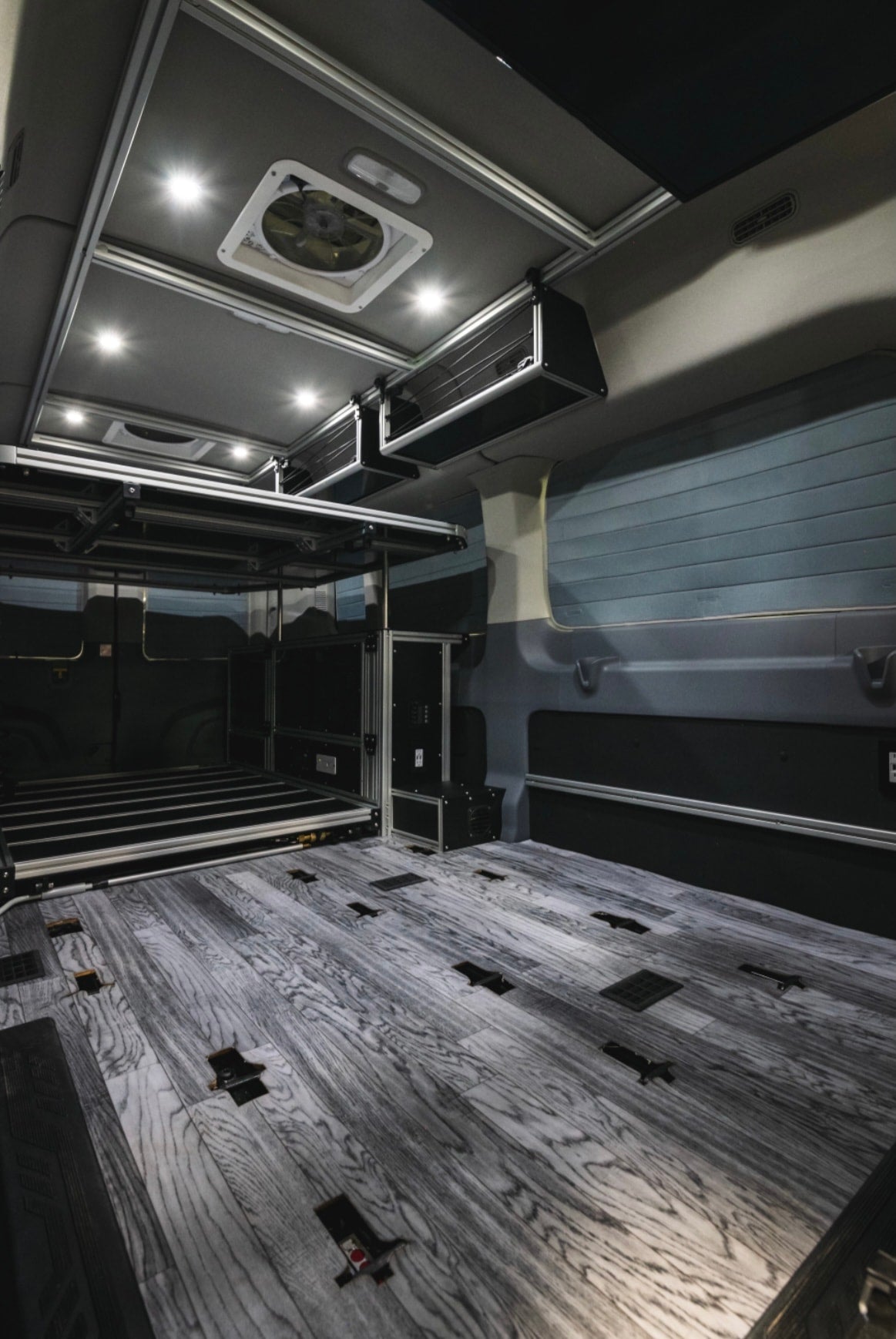 Modern RV rental interior: wood-look floor, elevated bed platform, overhead storage, and bright LED lighting. — photo 7