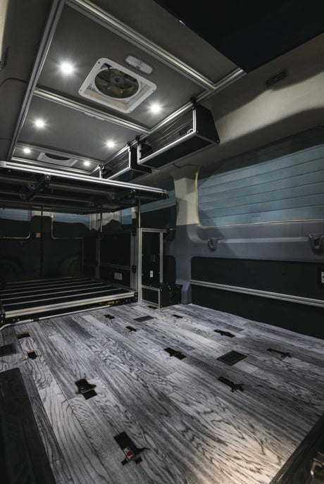 Modern RV rental interior: wood-look floor, elevated bed platform, overhead storage, and bright LED lighting.