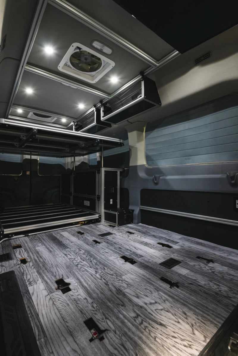 Modern RV rental interior: wood-look floor, elevated bed platform, overhead storage, and bright LED lighting. — photo 7