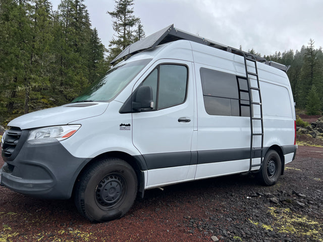 White Mercedes Sprinter campervan rv rental with roof solar and ladder, ready for adventures on a rocky trail.