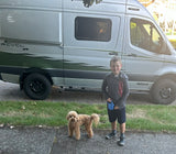 A young boy holds his curly-haired dog's leash beside a silver Winnebago Revel 4x4 rv rental, ready for adventure.