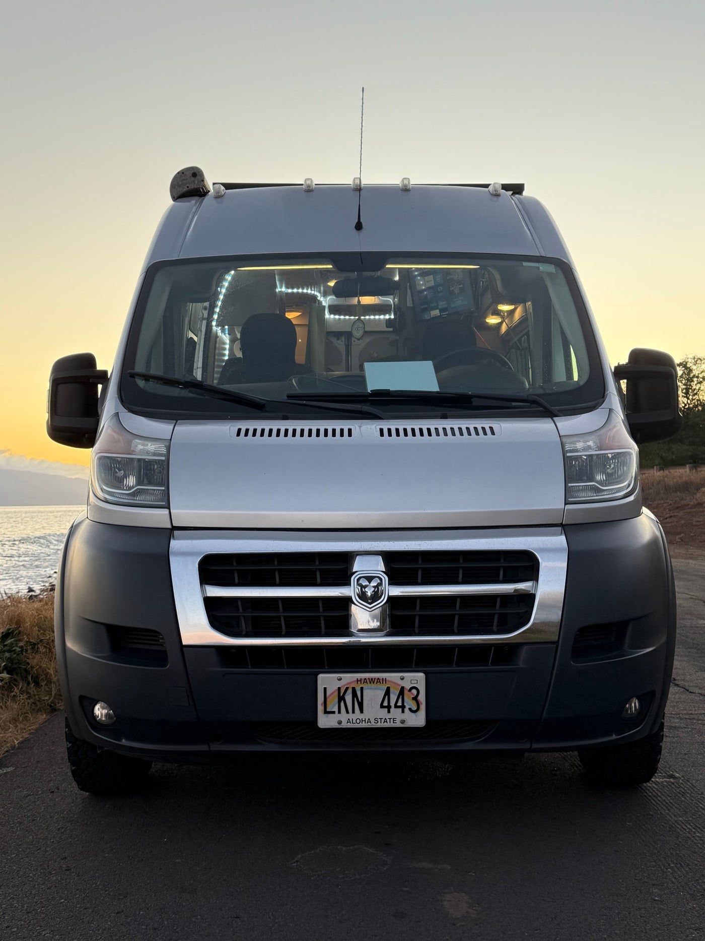 Front view of a silver camper van, ideal for RV rental adventures in Hawaii, parked with ocean views at sunset. — photo 4