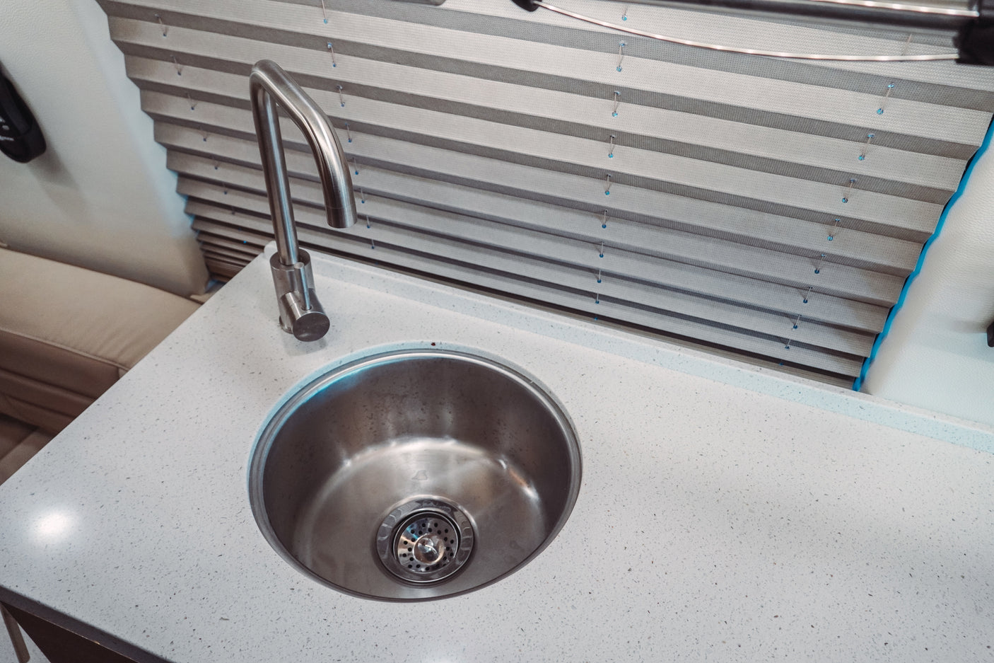 RV rental interior showing a clean kitchen sink, modern faucet, and white speckled countertop with privacy blinds.