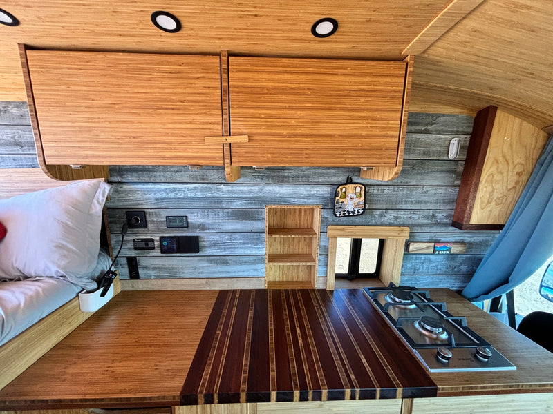 RV rental's inviting bamboo interior: organized kitchen with gas stove, overhead cabinets, and cozy sleeping area. — photo 11