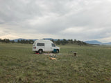 RV rental camper van set up for scenic outdoor camping in a vast grassy field with mountains.