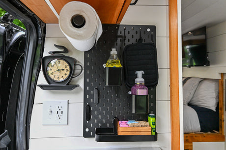 RV rental's clever interior organization: pegboard with kitchen essentials, clock, outlet, and cozy bed area view.