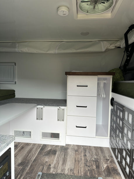 An rv rental interior featuring built-in storage, bed, and floor vents. A clean, functional camper living space.
