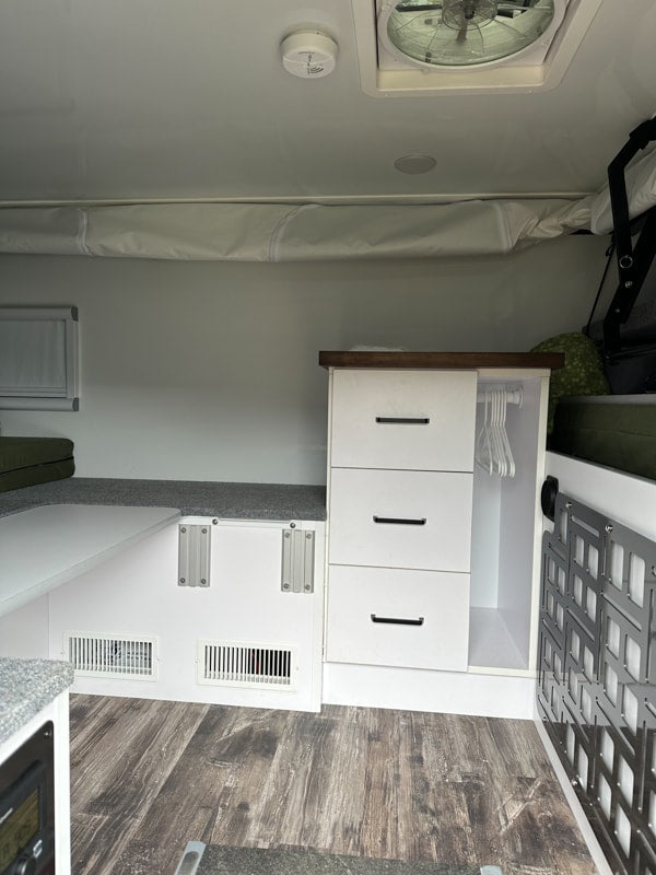 An rv rental interior featuring built-in storage, bed, and floor vents. A clean, functional camper living space. — photo 15