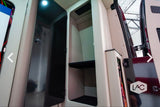 Modern RV rental interior with an open storage cabinet, featuring a sleek black door, an internal shelf, and organized wiring.