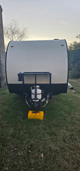 Front view of an RV rental travel trailer with its propane tank and hitch, parked on grass at dusk.