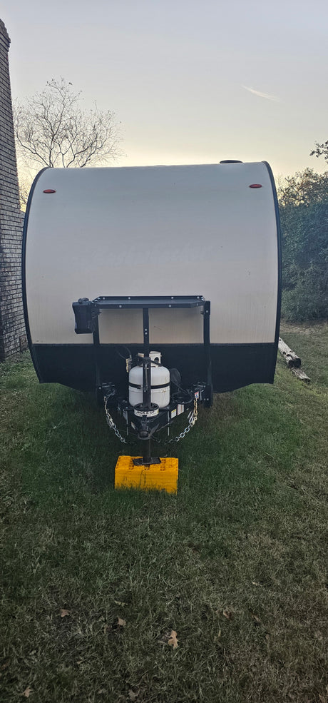 Front view of an RV rental travel trailer with its propane tank and hitch, parked on grass at dusk.