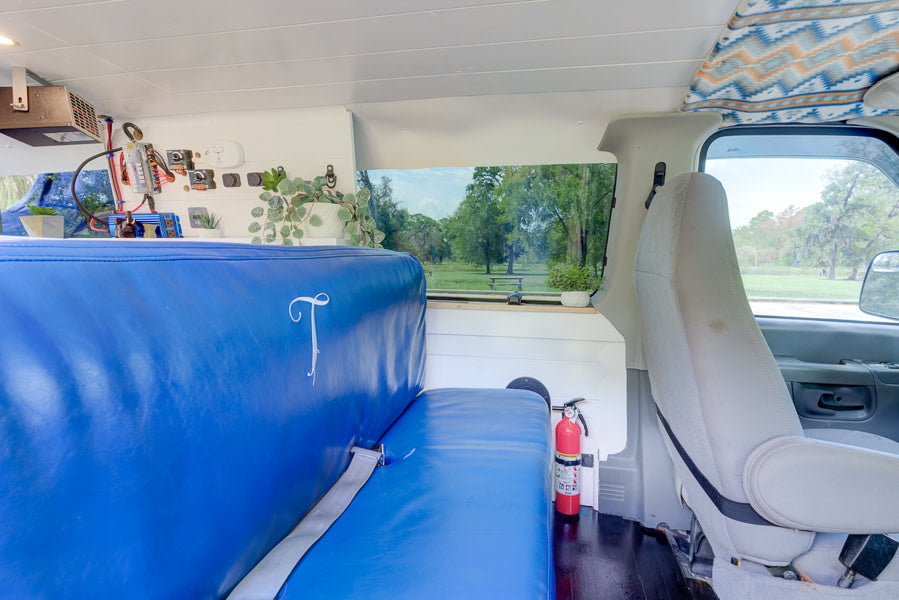 RV rental interior with blue seating, electrical components, fire extinguisher, and a park view from the window.