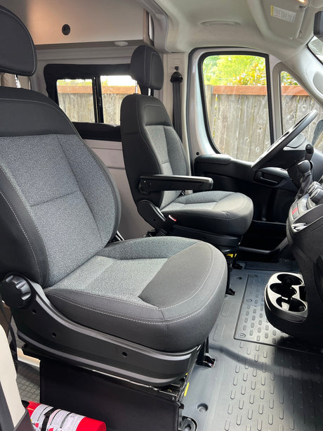Clean RV rental cabin with swivel front seats, steering wheel, and floor mats. Note the fire extinguisher.