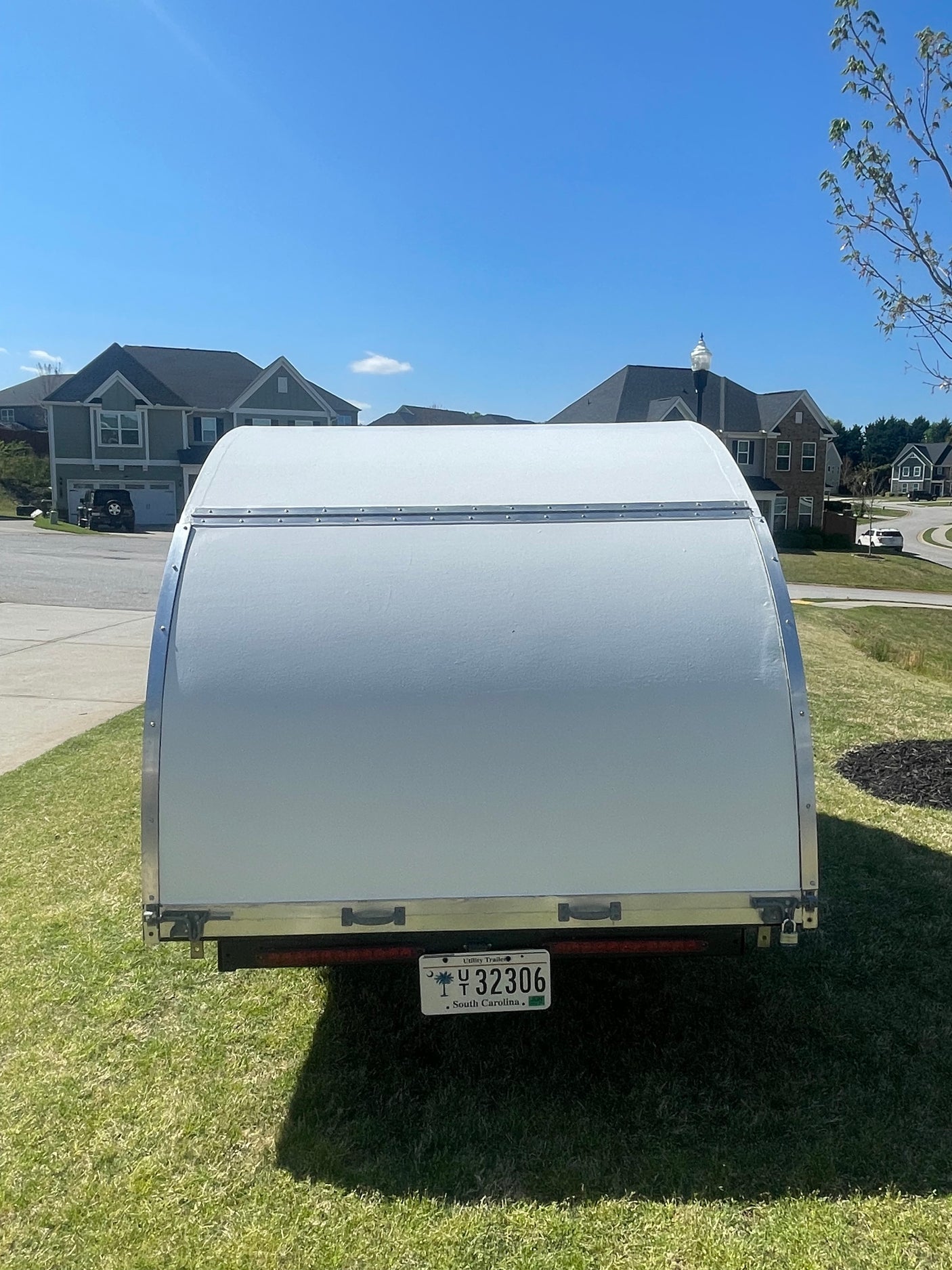 Rear of a white camper trailer available for RV rental, parked in a sunny South Carolina neighborhood. License Y 32306.