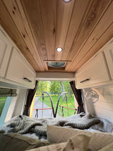 Cozy RV rental bedroom: wood ceiling, comfy bed, and a tranquil view of nature from the rear.