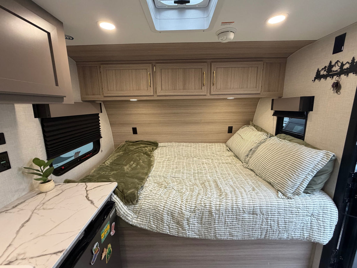  and overhead cabinets with a skylight.|A man and two dogs relax on a mat next to their Sportsmen RV rental at a leafy campsite — photo 4